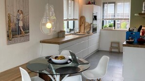 Eine moderne Küche mit weißen Schränken, einem runden Glastisch und weißen Stühlen. An der Wand hängt ein Gemälde und über dem Tisch eine Leuchte.