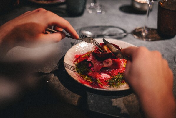 A person using a fork and knife to eat a dish with various food items on a plate. - Vaattunki Wilderness Resort (Rovaniemi)