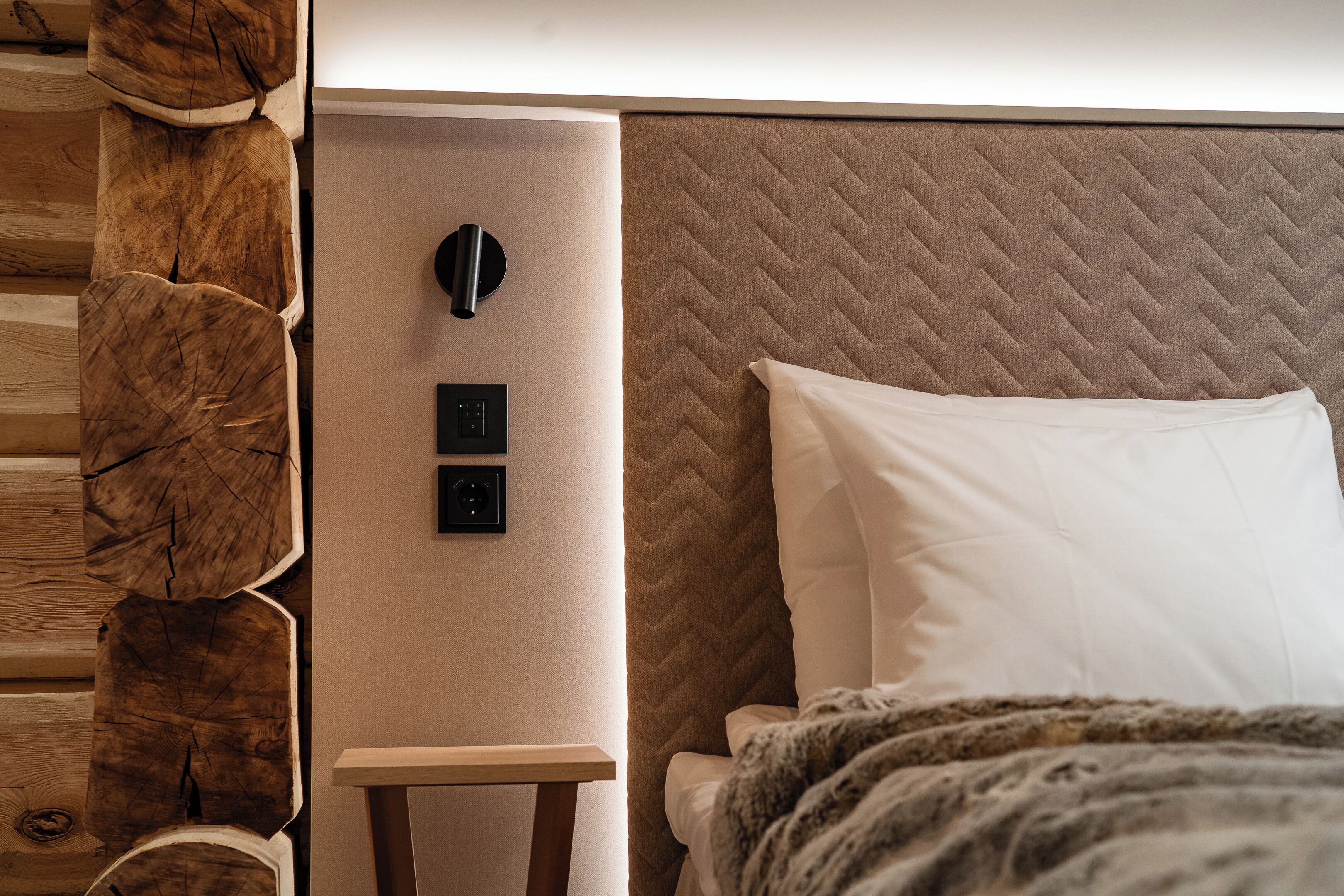 Un dormitorio moderno con pared de madera, una cama con cabecera acolchada y un panel de control junto a la cama.