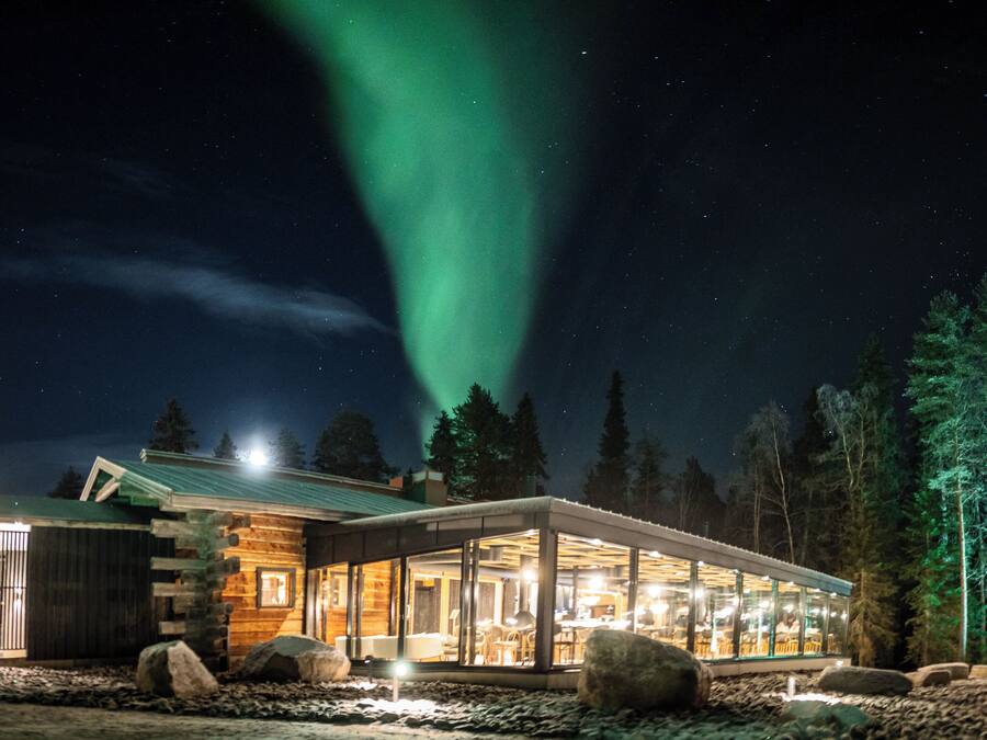 Una cabaña con fachada de vidrio, revestimiento de madera y vistas a la aurora boreal.