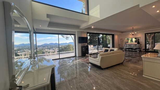 Ein geräumiger Wohnbereich mit einem großen Fenster und Blick auf die Stadt, einem modernen Sofa und einem Essbereich mit einer Chandelüster.