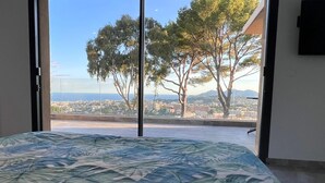 Ein Schlafzimmer mit großem Fenster und Blick auf die Stadt, inklusive Bäume und Gebäude.