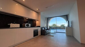 Eine moderne Küche mit Einbaugeräten, ein Essbereich mit einem Glastisch und Blick auf ein Schwimmbad durch große Fenster.