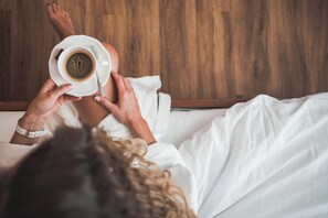 Une personne allongée dans son lit, tenant une tasse de café et une cuillère, et portant une chemise blanche.