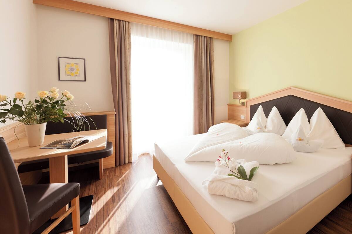 A hotel room with a bed, a desk, a chair, a nightstand, and a bedside table.