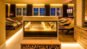A spa area with massage chairs, a heated stone bath, and a view of the night sky through large windows. - Hotel am Sonneck (Lagundo)