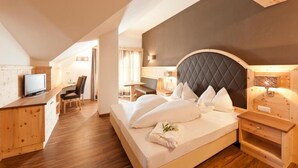 A hotel room with a large bed, a desk, a television, and a wooden floor. - Hotel am Sonneck (Lagundo)