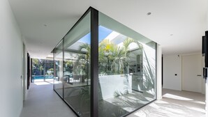 Un intérieur moderne avec une cloison en verre, une piscine et une vue sur les palmiers.