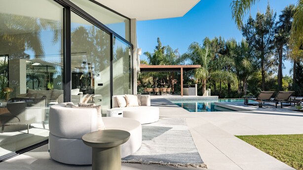 Un espace de vie extérieur moderne doté d’une piscine, de coins salon et d’un mur en verre.