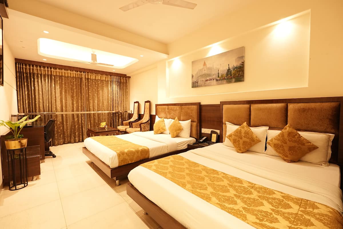 A hotel room with two beds, a desk, a chair, a plant, and a painting on the wall.