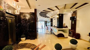 Un moderno vestíbulo de hotel con una recepción, un ascensor de vidrio y un suelo de mármol.