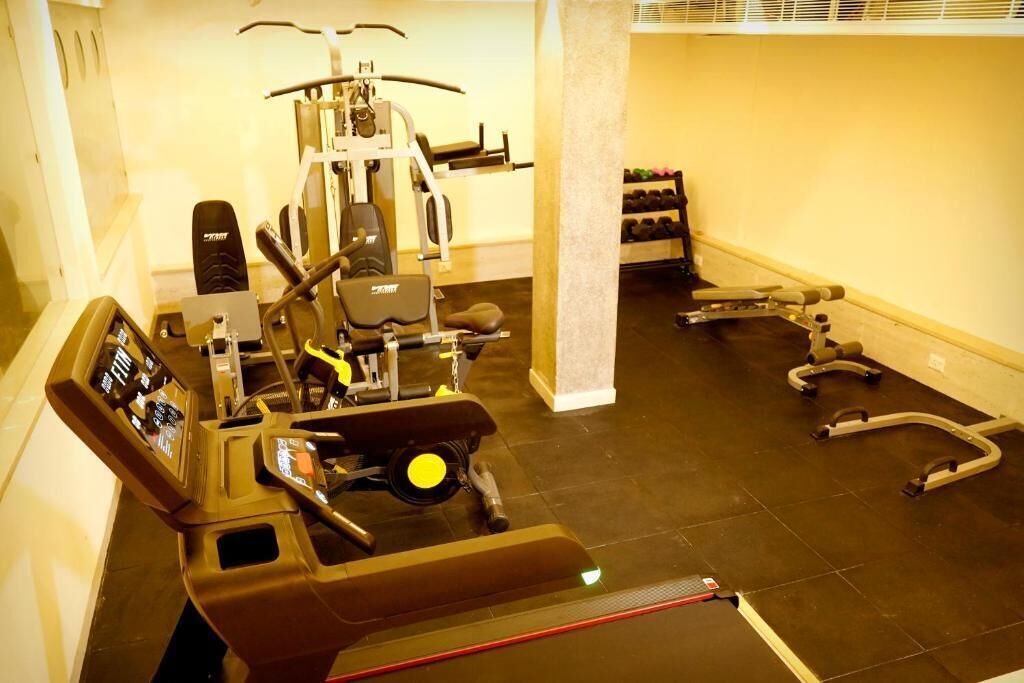 Un gimnasio con equipo de ejercicio diverso, incluyendo una cinta de correr, máquinas de pesas y mancuernas.