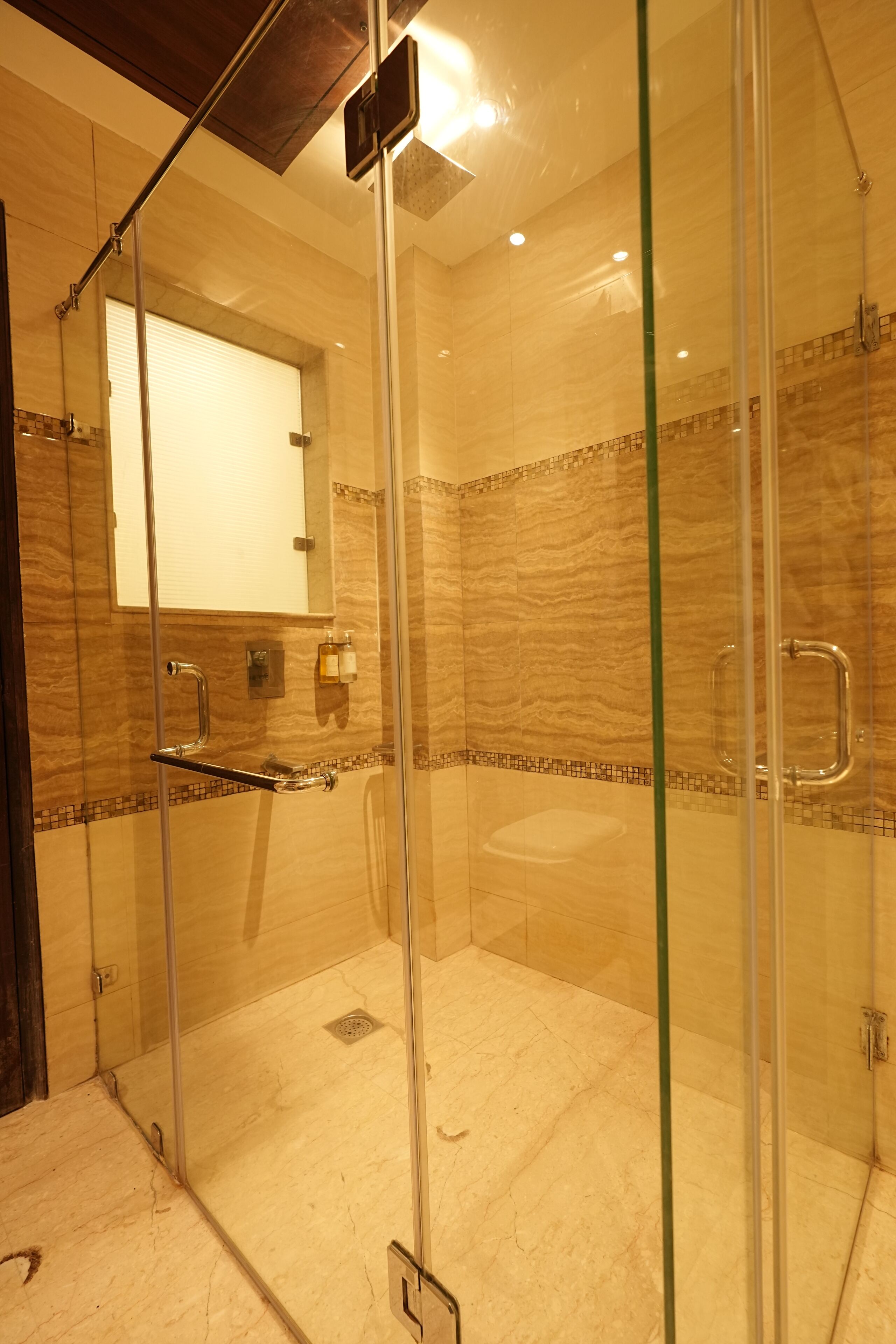 A glass-enclosed shower with a marble-tiled wall, a glass door, and a small mirror above the sink.