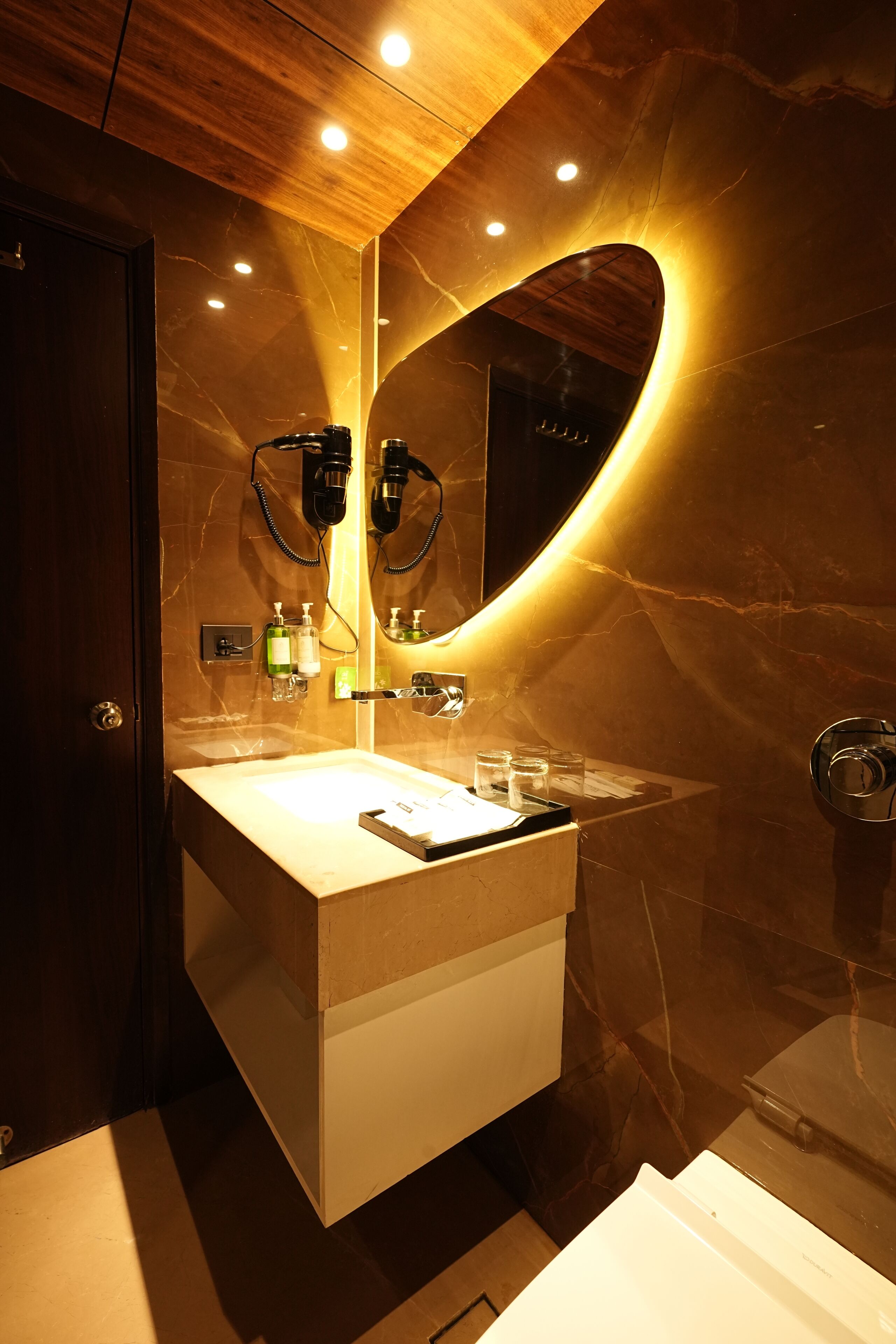 A modern bathroom with a marble vanity, a large mirror, and a hairdryer.