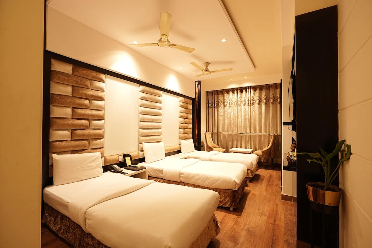 A hotel room with three beds, a wooden headboard, a ceiling fan, and a potted plant.