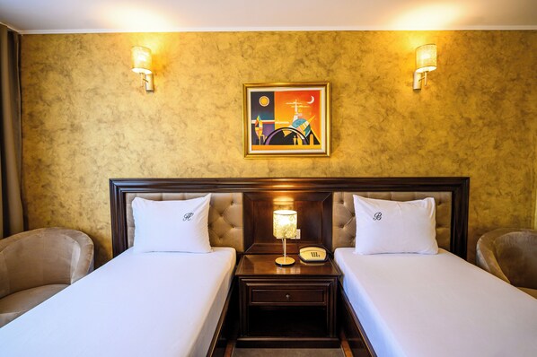 A hotel room with two beds, a nightstand with a lamp, and a painting on the wall. - Complex Bulevard (Constanta)