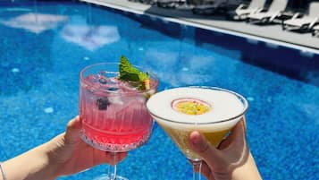 Due mani che sorreggono bicchieri da cocktail con una piscina sullo sfondo.