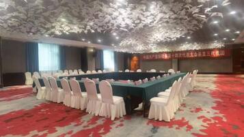 Un salón de conferencias con una larga mesa, sillas blancas y piso cubierto de alfombra roja.