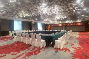 A conference room with a long table, white chairs, and a red carpeted floor.