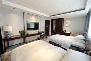 A hotel room with two beds, a desk with a lamp, a TV, and a wardrobe.