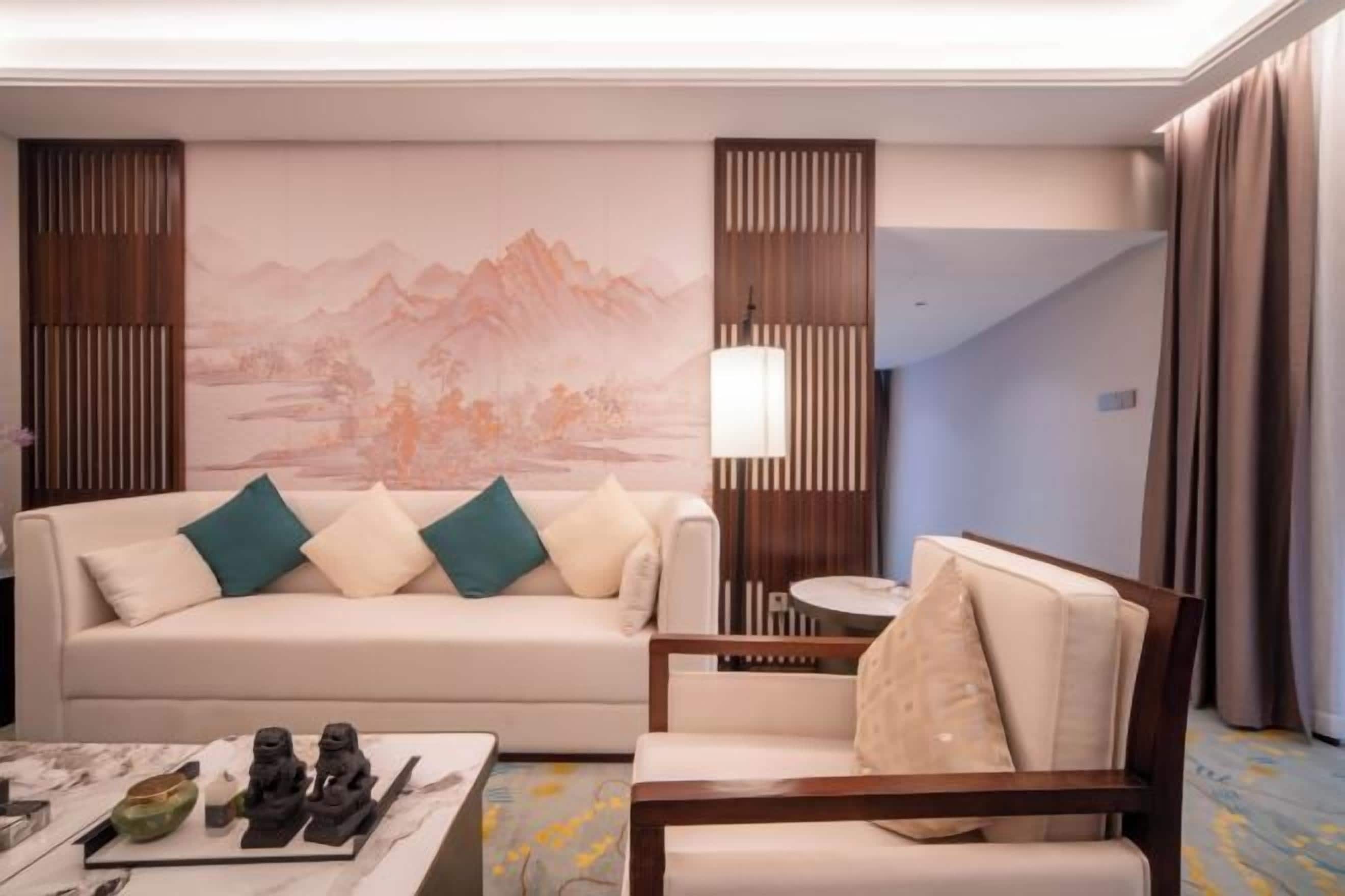 A hotel room with a sofa, armchair, and a table with decorative items.