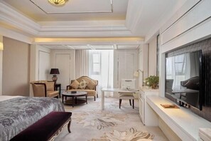 A hotel room with a large bed, a sofa, a desk, a television, and a window.