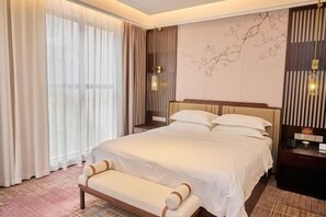 A hotel room with a large bed, a bench, a nightstand, and a wall with a tree design.