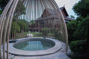 Un jacuzzi rodeado por una estructura de bambú, con un edificio tradicional al fondo.