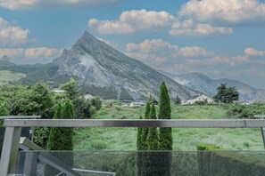Paesaggio montano con una cima imponente, un prato erboso e diverse case sullo sfondo.