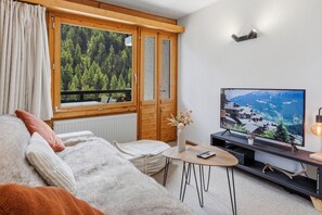 Ett mysigt vardagsrum med ett stort fönster, en tv och ett litet bord.