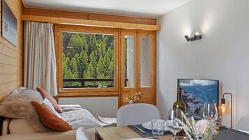 Ein gemütliches Zimmer mit Holzvertäfelung, einem Esstisch mit Stühlen, einem Fenster mit Blick auf einen Wald und einer Wandleuchte.