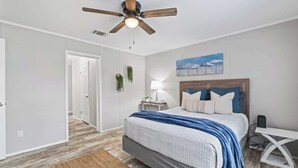 Ein Schlafzimmer mit einem Bett, einem Deckenventilator, einem Nachttisch, einem Schreibtisch und einem Bild an der Wand.