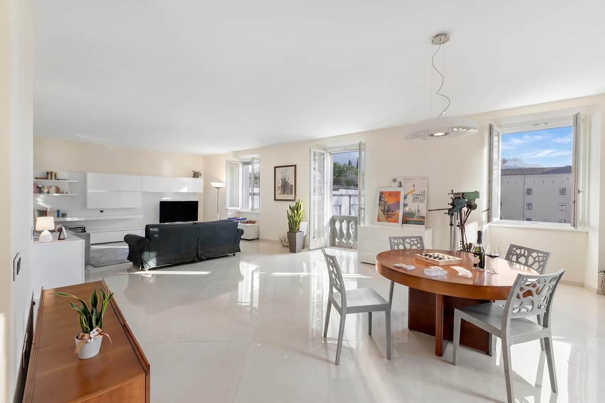 A spacious living area with a dining table, chairs, a sofa, and a kitchen in the background.