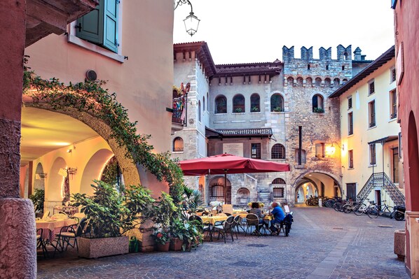 An outdoor café with tables and chairs, surrounded by stone buildings and a castle-like structure in the background.