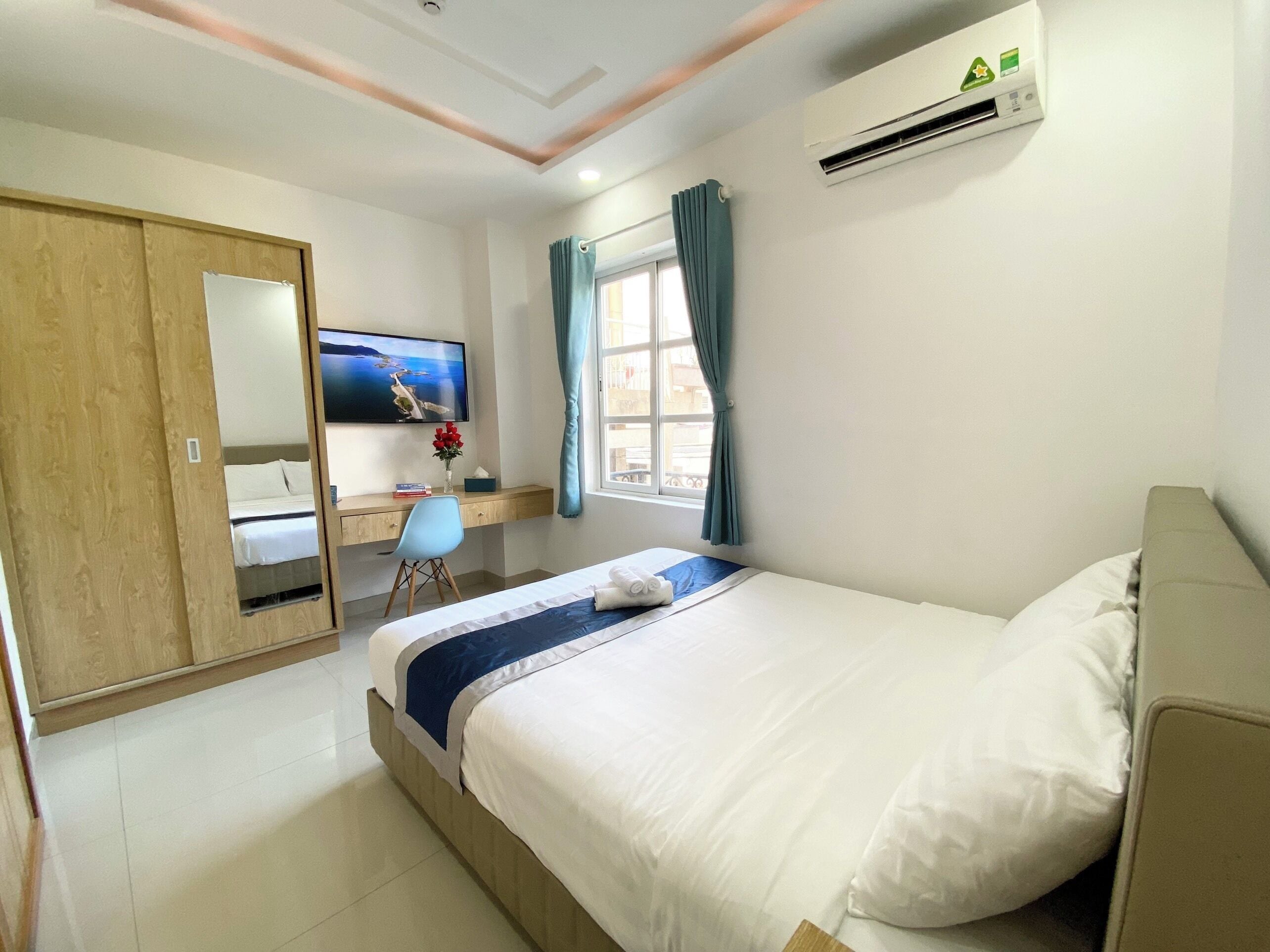 A hotel room with a bed, a desk, a TV, and an air conditioning unit.