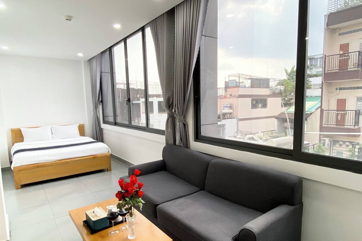 Habitación de hotel moderna con cama, sofá y un amplio ventanal con vistas a la ciudad.