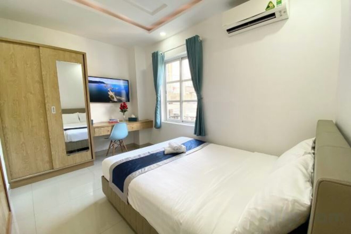 A hotel room with a bed, a desk, a chair, a TV, and a wardrobe.