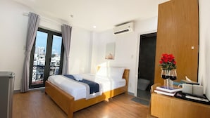 A hotel room with a wooden bed, a desk with a vase of flowers, and a view of the city through a balcony. - Home Away Minh Khai (Ho Chi Minh City)