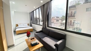A modern hotel room with a bed, a gray sofa, a wooden coffee table, and large windows offering a city view. - Home Away Minh Khai (Ho Chi Minh City)
