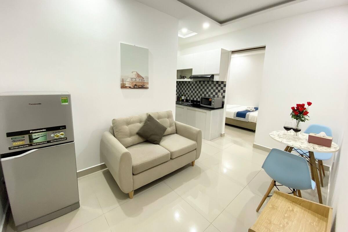 Una sala de estar moderna con un sofá, una mesa de comedor con sillas, una zona de cocina y un refrigerador.