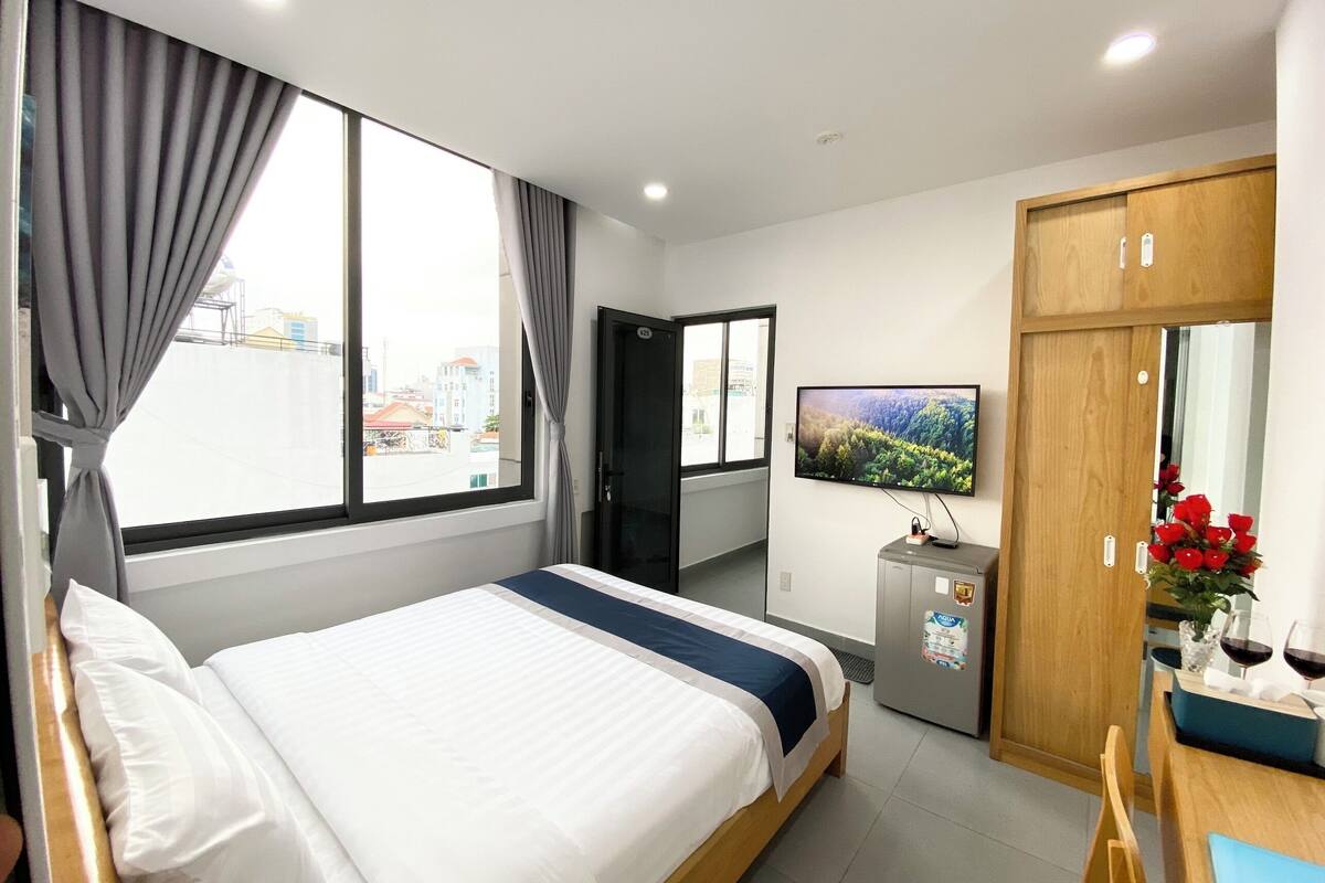 Habitación de hotel con cama, televisión, pequeño refrigerador, armario de madera y vistas a la ciudad.