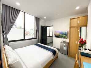 A hotel room with a bed, a TV, a small fridge, a wooden wardrobe, and a view of the city. - Home Away Minh Khai (Ho Chi Minh City)