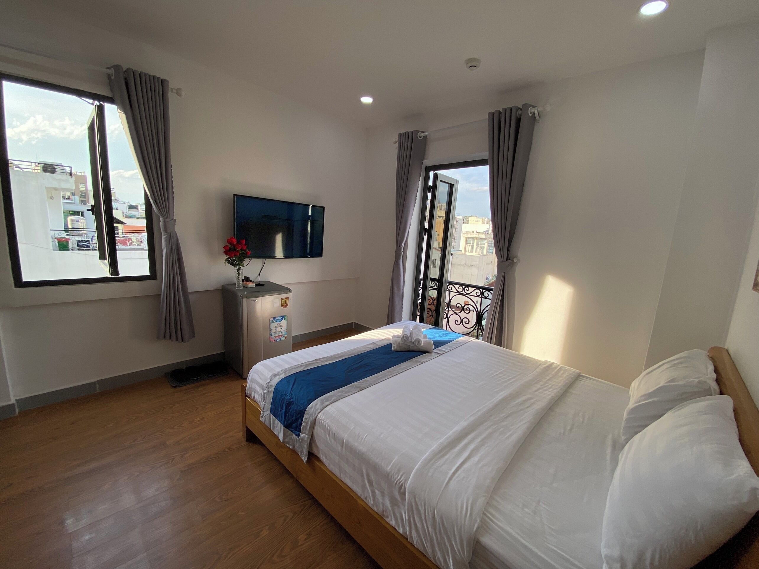 Hotellihuone, jossa on sänky, televisio, minibaari ja ikkuna, jossa on verhot.
