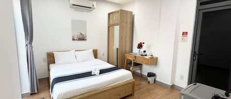 Habitación de hotel con cama de madera, un escritorio con silla, aire acondicionado, armario y una puerta.