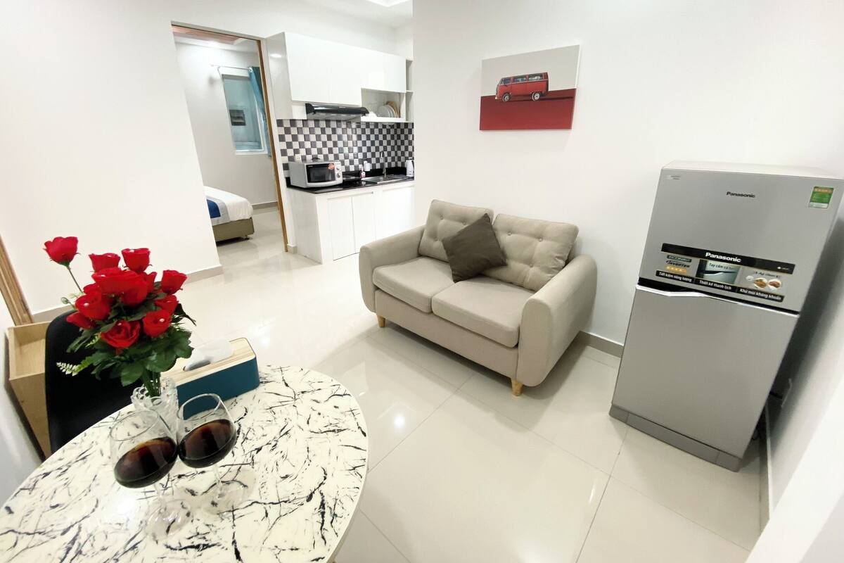 Una sala moderna con una mesa de centro de mármol, un sofá color beige y una zona de cocina con armarios blancos y una obra de arte roja en la pared.