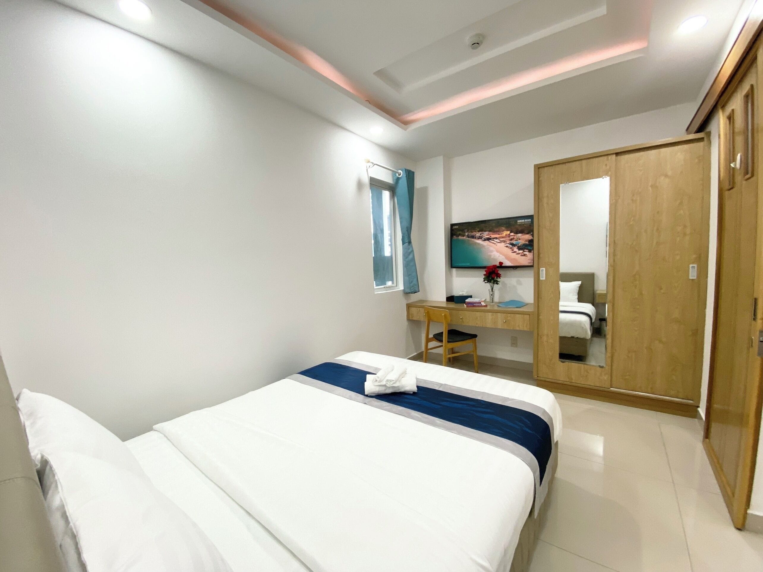 A hotel room with a bed, a desk, a chair, a TV, and a wardrobe.