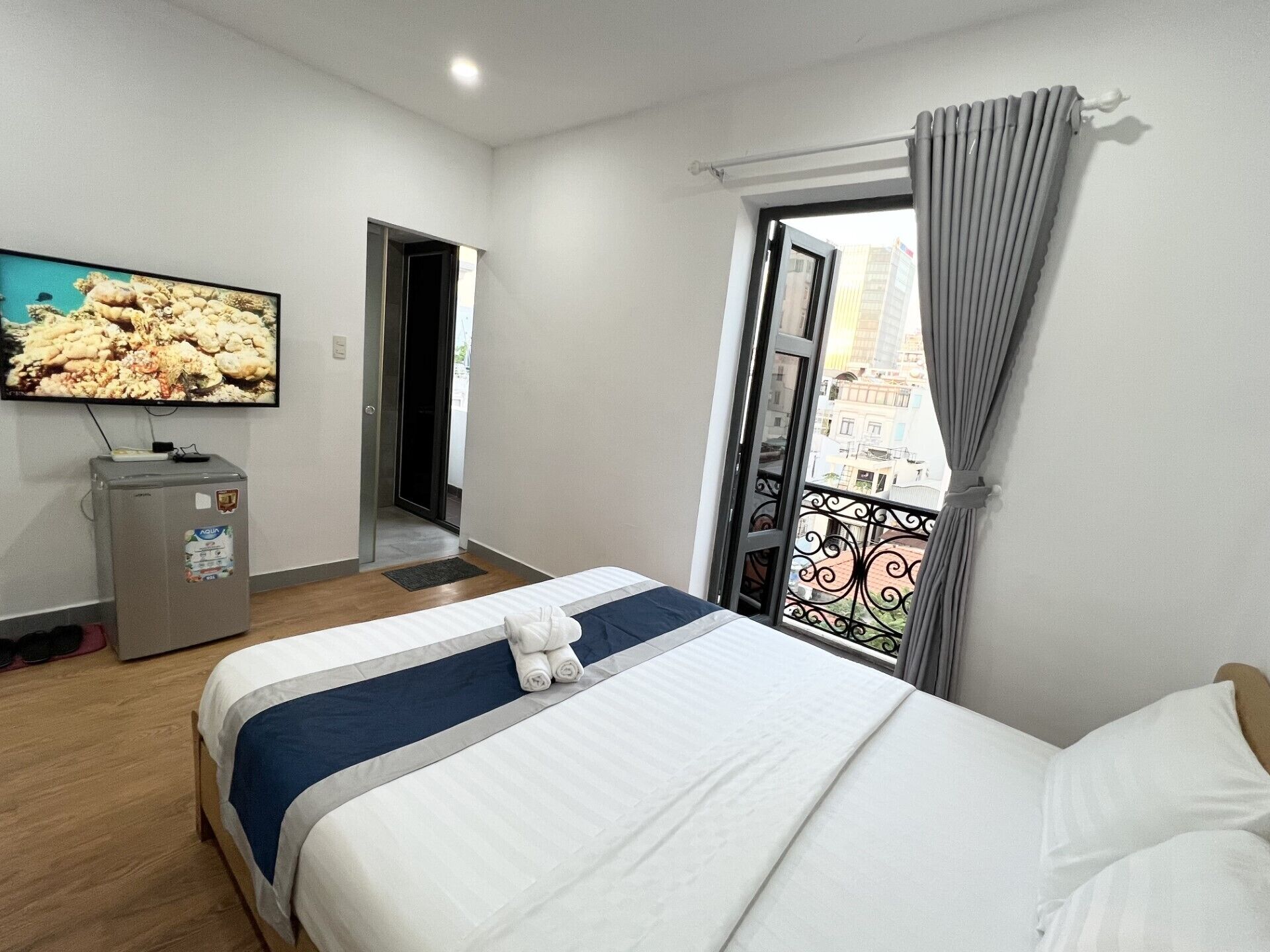 Une chambre d’hôtel équipée d’un lit, d’une télévision, d’un minibar et d’un balcon avec vue sur les bâtiments.