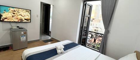 Une chambre d’hôtel équipée d’un lit, d’une télévision, d’un minibar et d’un balcon avec vue sur les bâtiments.