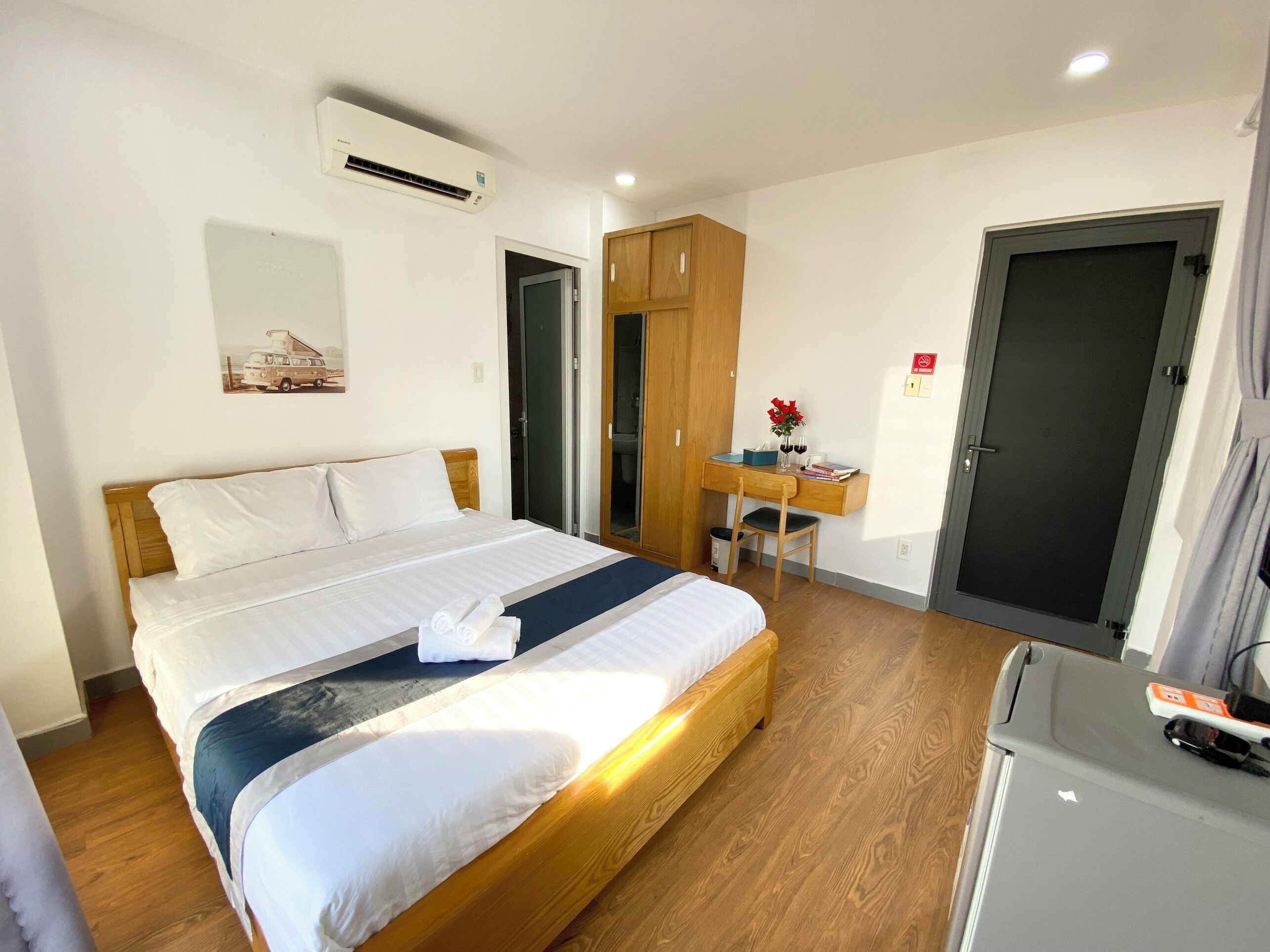 Hotelkamer met een houten bed, een bureau met stoel, een kleine koelkast en een deur.