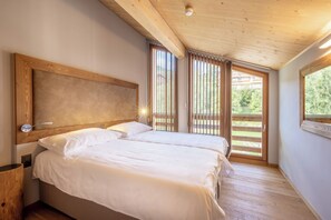 A bedroom with two beds, wooden ceiling beams, a large window, and a view of greenery outside. - SWISSPEAK Resorts by Pierre & Vacances Premium Vercorin (Chalais)